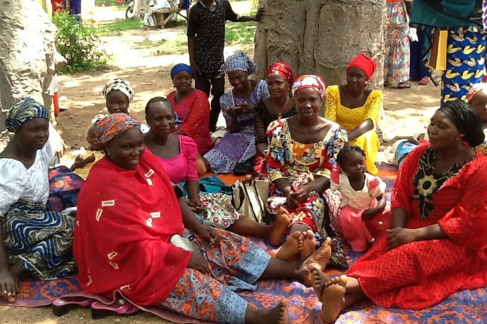 Nigerian women sitting together outdoors during a community discussion.