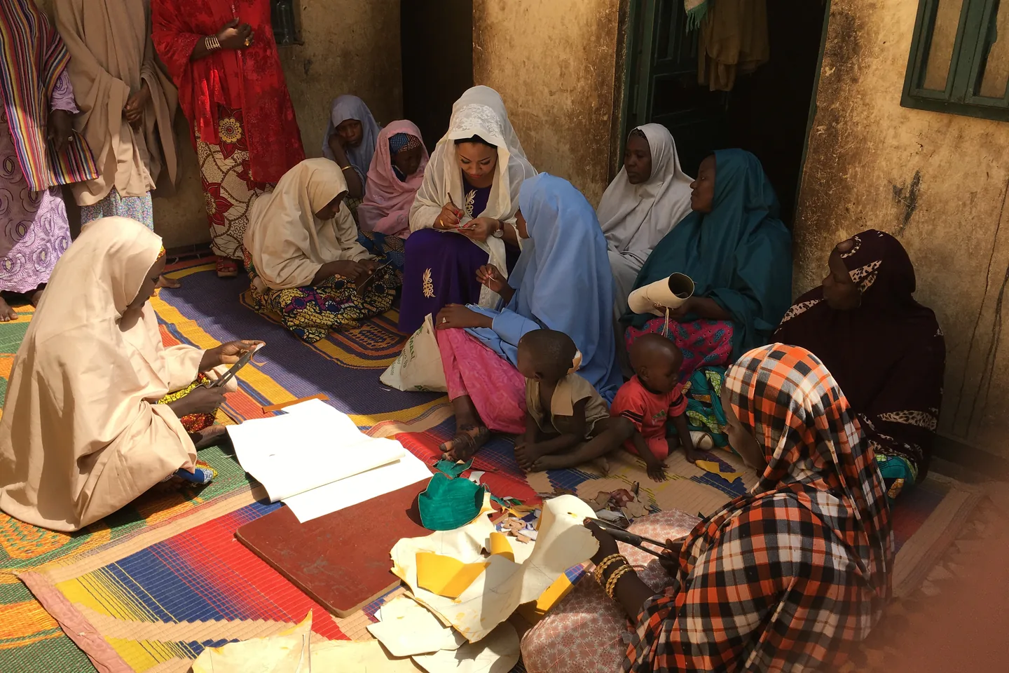 Women artisans in northern Nigeria working together with leather pattern pieces in a courtyard.
